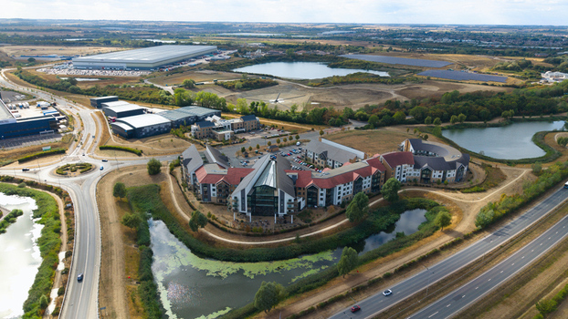 Aerial view of Wixams Retirement Village featuring unique modern architecture with pitched roofs surrounded by landscaped grounds small lakes and nearby roads in Bedford England United Kingdom.
