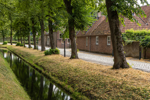 View of a quiet cobblestone street lined with mature trees and a narrow canal in the historic town of Heusden North Brabant Netherlands.