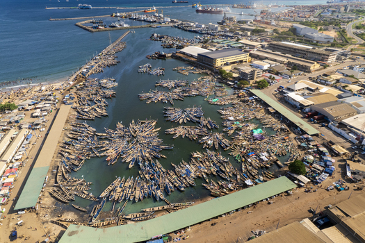 Aerial view of boats clustered in the harbor casting long shadows on the water against the backdrop of the industrial buildings Tema Ghana. Aerial view of boats clustered in the harbor casting long shadows on the water against the backdrop of the industrial buildings Tema Ghana.