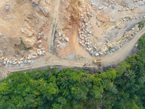 Aerial view of a mining site with large rocks dirt roads and a truck driving through the landscape bordered by dense green forest in Bukit Tambun Penang Malaysia. Aerial view of a mining site with large rocks dirt roads and a truck driving through the landscape bordered by dense green forest in Bukit Tambun Penang Malaysia.