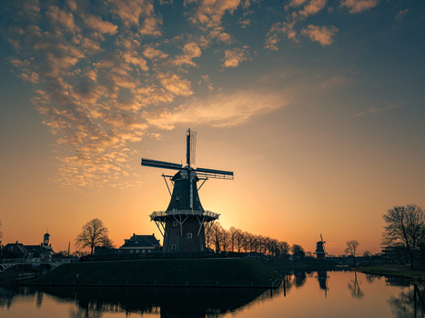 Aerial view of a traditional Dutch windmill silhouette against a golden sunset sky with scattered clouds and water reflections in Dokkum Friesland Netherlands. Aerial view of a traditional Dutch windmill silhouette against a golden sunset sky with scattered clouds and water reflections in Dokkum Friesland Netherlands.
