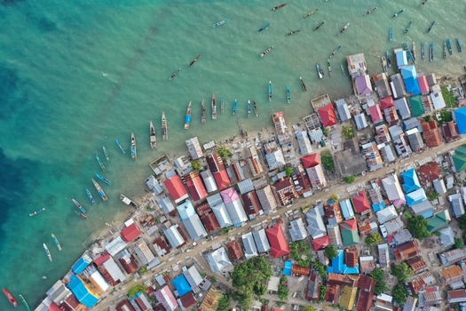 Aerial view of Pulau Maginti showing a coastal village with colorful houses and wooden boats moored in clear turquoise water in Maginti South East Sulawesi Indonesia.
