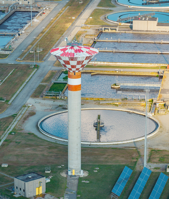 Aerial view of a wastewater treatment plant featuring a tall red and white water tower circular clarifiers and solar panels in ITALY.