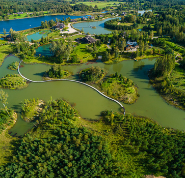 Aerial view of a winding wooden footbridge connecting small islands in a lake surrounded by lush green forests and meadows in Latvia. Aerial view of a winding wooden footbridge connecting small islands in a lake surrounded by lush green forests and meadows in Latvia.