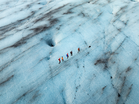 Aerial view of hikers trekking across the blue ice of Breidamerkurjokull glacier with visible crevasses and dark volcanic ash streaks in Sveitarfelagid Hornafjordur Iceland. Aerial view of hikers trekking across the blue ice of Breidamerkurjokull glacier with visible crevasses and dark volcanic ash streaks in Sveitarfelagid Hornafjordur Iceland.