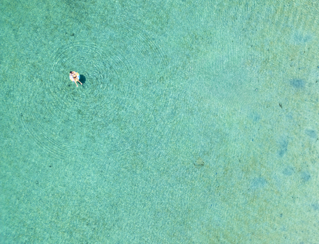 Aerial view of a person relaxing on an inflatable ring in the crystal clear turquoise waters of the Caribbean Sea in Guanaja Bay Islands Department Honduras. Aerial view of a person relaxing on an inflatable ring in the crystal clear turquoise waters of the Caribbean Sea in Guanaja Bay Islands Department Honduras.