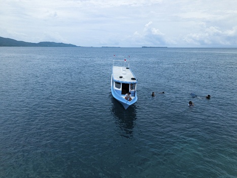 Aerial view of a boat floating on the deep blue sea with people swimming nearby at Cemara Kecil Snorkeling Spot Karimunjawa Central Java Indonesia.