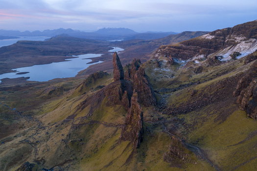 Aerial view of The Storr rock formation with its iconic jagged pinnacles overlooking the calm waters of Loch Leathan under a soft morning sky in Isle of Skye Scotland United Kingdom. Aerial view of The Storr rock formation with its iconic jagged pinnacles overlooking the calm waters of Loch Leathan under a soft morning sky in Isle of Skye Scotland United Kingdom.