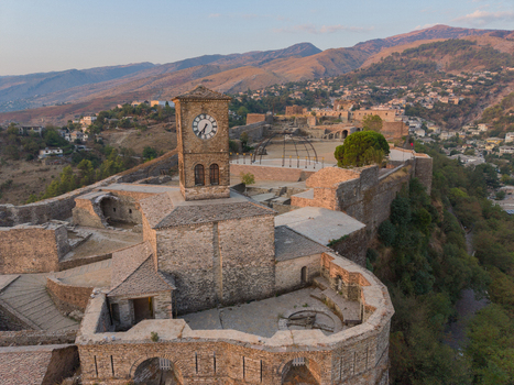 Aerial view of Gjirokaster Castle featuring its iconic clock tower stone fortifications and historic walls overlooking the surrounding mountains in Gjirokaster Gjirokaster County Albania. Aerial view of Gjirokaster Castle featuring its iconic clock tower stone fortifications and historic walls overlooking the surrounding mountains in Gjirokaster Gjirokaster County Albania.