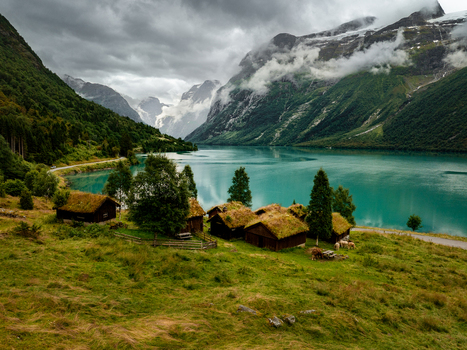 Aerial view of Lovatnet lake surrounded by mountains and traditional wooden cabins with grass roofs in Stryn Municipality Vestland Norway.