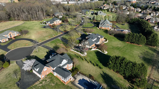 Aerial view of a residential neighborhood featuring large brick houses with dark roofs manicured lawns winding driveways and swimming pools in Forest Virginia United States.