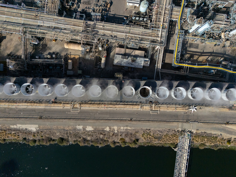 Aerial view of industrial cooling towers with steam rising from circular fans at a refinery facility in Carson California United States.