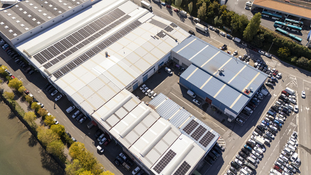 Aerial view of industrial warehouses with solar panels on the roofs a large parking lot filled with cars and adjacent roads in Zumaia Basque Country Spain.