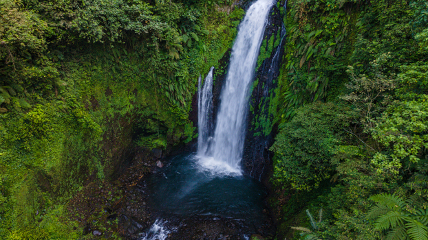 Aerial view of Gomblang Waterfall cascading into a turquoise pool surrounded by lush tropical rainforest and mossy cliffs Kecamatan Kedungbanteng Jawa Tengah Indonesia. Aerial view of Gomblang Waterfall cascading into a turquoise pool surrounded by lush tropical rainforest and mossy cliffs Kecamatan Kedungbanteng Jawa Tengah Indonesia.