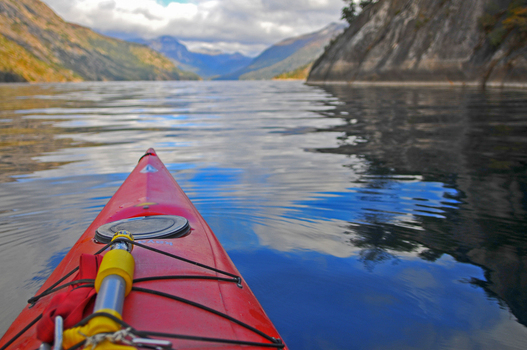 View of a red kayak on the calm waters of Nahuel Huapi Lake surrounded by steep mountains under a cloudy sky San Carlos de Bariloche Rio Negro Argentina. View of a red kayak on the calm waters of Nahuel Huapi Lake surrounded by steep mountains under a cloudy sky San Carlos de Bariloche Rio Negro Argentina.