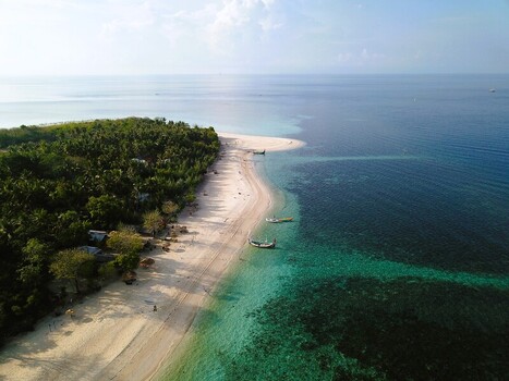 Aerial view of a tropical beach with turquoise water white sand lush palm trees and traditional boats moored along the shore in Sumenep East Java Indonesia.
