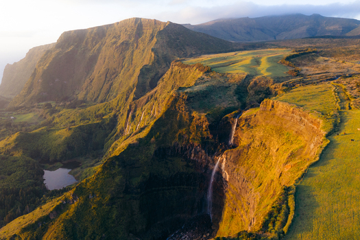 Aerial view of Poco da Ribeira do Ferreiro waterfalls cascading down steep green cliffs during golden hour in Fajazinha Azores Portugal. Aerial view of Poco da Ribeira do Ferreiro waterfalls cascading down steep green cliffs during golden hour in Fajazinha Azores Portugal.