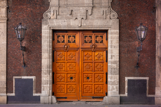 View of ornate carved wooden doors flanked by vintage lanterns on a historic stone facade in Mexico City Mexico City Mexico.
