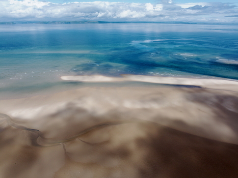 Aerial view of the Moray Firth Coast featuring expansive sandy beaches tidal channels and clear blue waters under a cloudy sky in Nairn Scotland United Kingdom.
