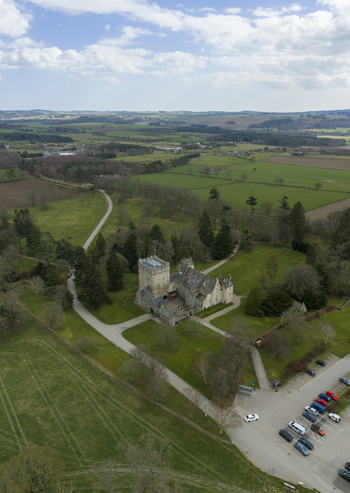 Aerial view of Drum Castle with its historic stone tower surrounded by lush green lawns woodland and rolling countryside Drumoak Scotland United Kingdom.