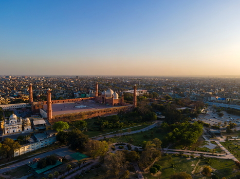 Aerial view of Badshahi Mosque with its red sandstone walls and white marble domes surrounded by lush gardens and the sprawling urban landscape of Lahore Punjab Pakistan. Aerial view of Badshahi Mosque with its red sandstone walls and white marble domes surrounded by lush gardens and the sprawling urban landscape of Lahore Punjab Pakistan.