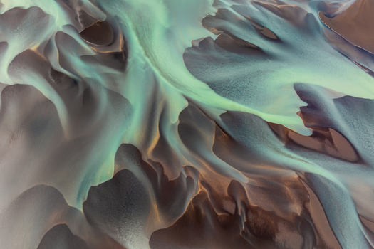 Aerial view of a glacial river with turquoise sediment rich water flowing through dark volcanic sand patterns in Iceland. Aerial view of a glacial river with turquoise sediment rich water flowing through dark volcanic sand patterns in Iceland.