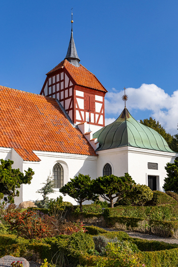 View of the historic church in Hindsholm with its distinctive red timber framed tower and green dome set within a manicured garden in Kerteminde Kerteminde Municipality Denmark. View of the historic church in Hindsholm with its distinctive red timber framed tower and green dome set within a manicured garden in Kerteminde Kerteminde Municipality Denmark.