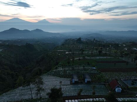 Aerial view of terraced agricultural fields and distant mountains at sunrise in Kecamatan Kaliangkrik Jawa Tengah Indonesia. Aerial view of terraced agricultural fields and distant mountains at sunrise in Kecamatan Kaliangkrik Jawa Tengah Indonesia.