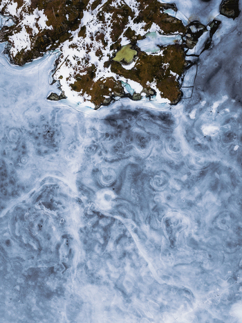 Aerial view of the stark contrast between snow dusted land and swirling icy waters creates a mesmerizing dance of textures and tones Tind Nordland Norway.