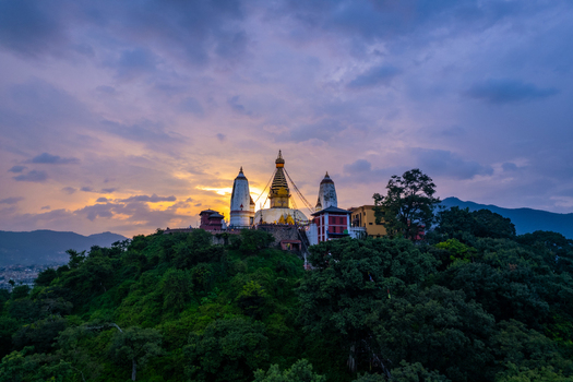 Aerial view of the Swayambhunath Stupa perched on a lush green hill at sunset with golden light illuminating the iconic dome and surrounding structures in Nepal.