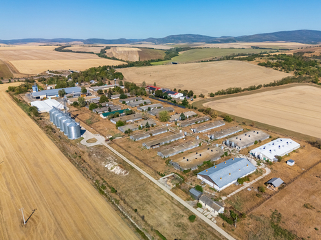 Aerial view of farm buildings grain silos and livestock barns near Paszto Nograd County Hungary surrounded by farmland crop fields and hills in a rural agricultural landscape. Aerial view of farm buildings grain silos and livestock barns near Paszto Nograd County Hungary surrounded by farmland crop fields and hills in a rural agricultural landscape.