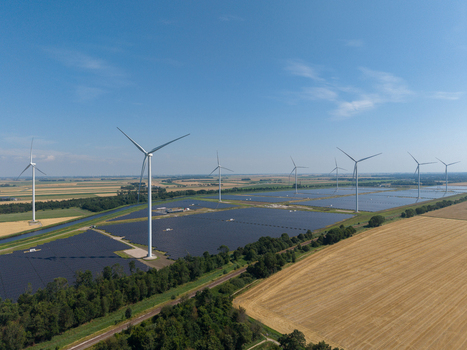 Aerial view of a large solar farm and wind turbines set within a rural landscape of agricultural fields and green trees in the Netherlands.