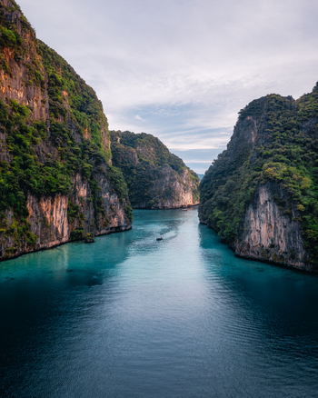 Aerial view of Pi Leh Bay with turquoise water towering limestone cliffs lush vegetation and a small boat in the center in Tambon Ao Nang Chang Wat Krabi Thailand. Aerial view of Pi Leh Bay with turquoise water towering limestone cliffs lush vegetation and a small boat in the center in Tambon Ao Nang Chang Wat Krabi Thailand.