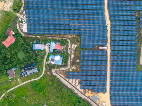 Aerial view of large scale solar photovoltaic power plant with rows of solar panels adjacent to rural houses palm trees and dirt paths in Central Seberang Perai Penang Malaysia. Aerial view of large scale solar photovoltaic power plant with rows of solar panels adjacent to rural houses palm trees and dirt paths in Central Seberang Perai Penang Malaysia.