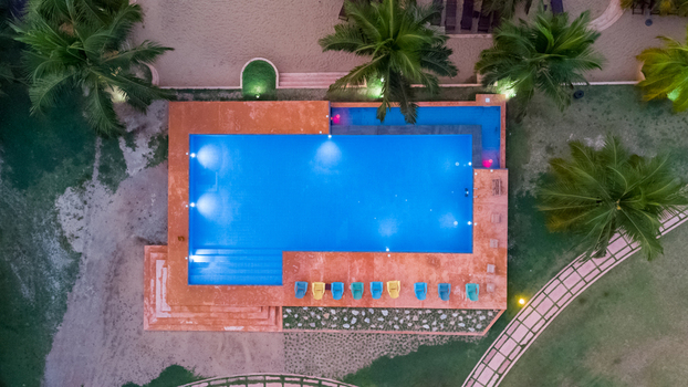 Axim Ghana 09 February 2023 Aerial view of the swimming pool at Lou Moon Resort featuring vibrant blue water surrounding palm trees and colorful lounge chairs on the deck. Axim Ghana 09 February 2023 Aerial view of the swimming pool at Lou Moon Resort featuring vibrant blue water surrounding palm trees and colorful lounge chairs on the deck.