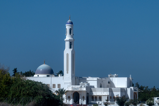 View of a white mosque with a prominent minaret and dome set against a clear blue sky in Muscat Muscat Governorate Oman. View of a white mosque with a prominent minaret and dome set against a clear blue sky in Muscat Muscat Governorate Oman.