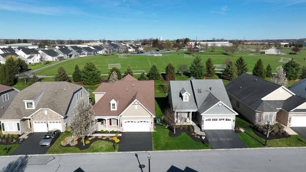 Aerial view of suburban houses with asphalt driveways and manicured lawns bordering a large green park with soccer fields in Mount Joy Pennsylvania United States.