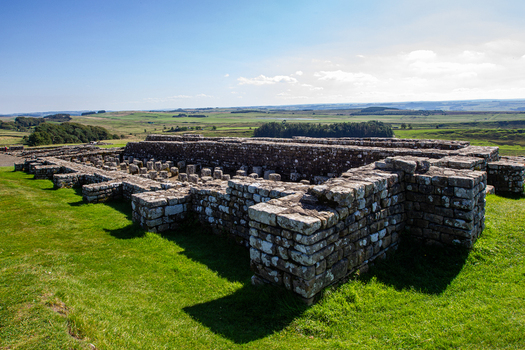 View of the ancient Roman stone ruins of Vindolanda fort with green grass and rolling hills under a bright sky Hexham England United Kingdom. View of the ancient Roman stone ruins of Vindolanda fort with green grass and rolling hills under a bright sky Hexham England United Kingdom.
