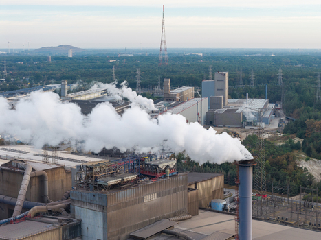 Aerial view of the industrial manufacturing complex in Genk Zuid with smoking chimneys and steel production facilities surrounded by forest in Genk Vlaanderen Belgium. Aerial view of the industrial manufacturing complex in Genk Zuid with smoking chimneys and steel production facilities surrounded by forest in Genk Vlaanderen Belgium.