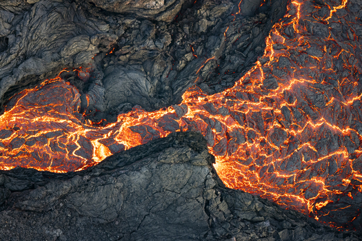 Aerial view of molten lava snaking through the dark textured volcanic rock of the Reykjanes Peninsula a fiery dance of destruction and creation Grindav&iacute;kurb&aelig;r Iceland.