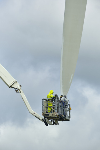 Esbjerg Syddanmark Denmark 24 July 2026 View of crew performing maintenance on a wind turbine blade using a high reaching cherry picker against a cloudy sky.