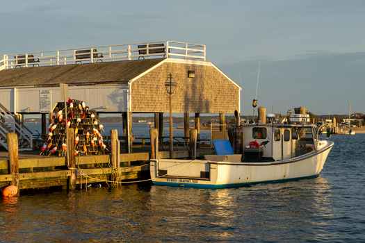 View of a fishing boat docked at a wooden pier with lobster traps and a shingled building during golden hour in Edgartown Massachusetts United States.