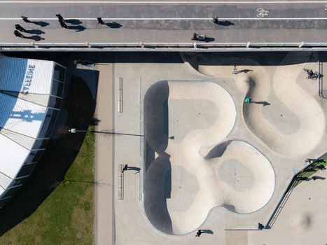 Aerial view of the skatepark at Chiune Sugihara Sakura Park with concrete bowls surrounding grass and people walking on the adjacent path in Vilnius Vilniaus apskritis Lithuania. Aerial view of the skatepark at Chiune Sugihara Sakura Park with concrete bowls surrounding grass and people walking on the adjacent path in Vilnius Vilniaus apskritis Lithuania.