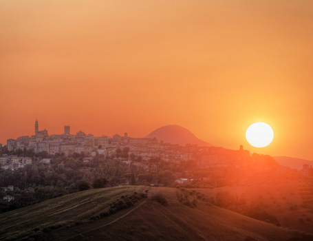 View of the historic town of Mogliano perched on a hill during a vibrant golden hour sunset with rolling landscape in the foreground in Mogliano Marche Italy.