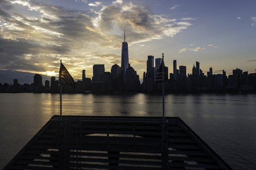 Aerial view of the New York City skyline featuring One World Trade Center at sunset with American flags waving on a pier in New York New York United States.
