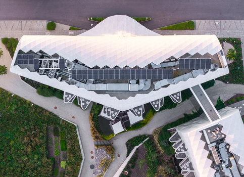 Aerial view of the modern medical resort featuring a white geometric roof with solar panels surrounded by lush greenery and paved pathways in Sopot Pomeranian Voivodeshi Poland. Aerial view of the modern medical resort featuring a white geometric roof with solar panels surrounded by lush greenery and paved pathways in Sopot Pomeranian Voivodeshi Poland.