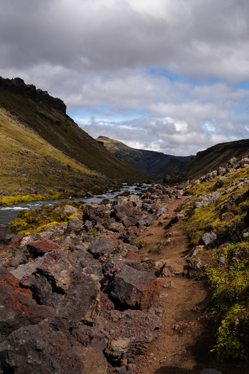 View of a rugged trail winding through a volcanic valley with the dark lava rocks contrasting against the green moss and a river flowing Skaftárhreppur Iceland. View of a rugged trail winding through a volcanic valley with the dark lava rocks contrasting against the green moss and a river flowing Skaftárhreppur Iceland.