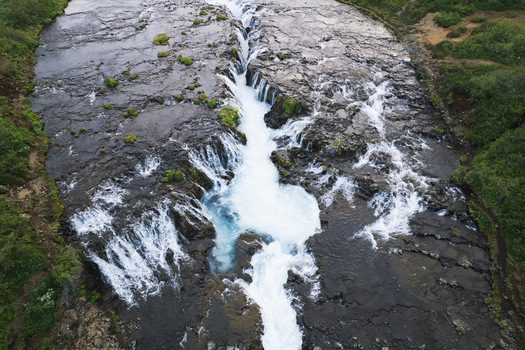 Aerial view of the turquoise waters of Bruarfoss waterfall cascading through dark volcanic rock formations and lush green banks Blaskogabyggd Iceland. Aerial view of the turquoise waters of Bruarfoss waterfall cascading through dark volcanic rock formations and lush green banks Blaskogabyggd Iceland.