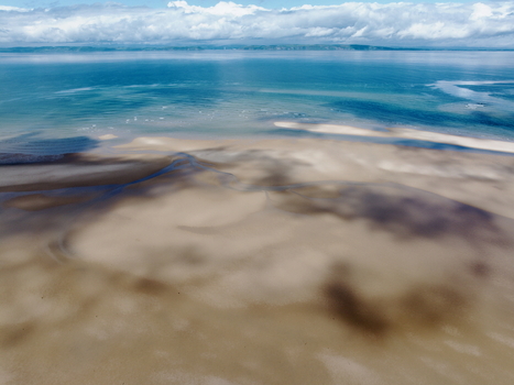 Aerial view of the Moray Firth Coast featuring expansive sandy tidal flats shallow turquoise waters and dramatic cloud shadows cast across the beach in Nairn Scotland United Kingdom.