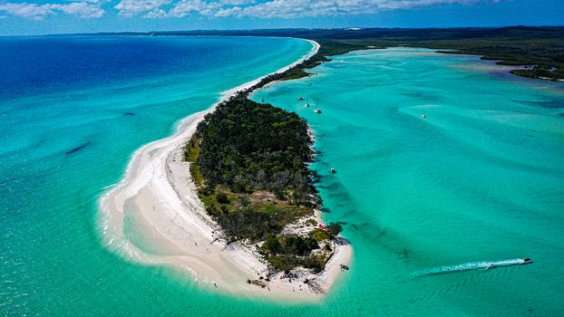 Aerial view of turquoise waters and white sandy beaches surrounding the island featuring lush vegetation and boats anchored in the clear shallows in K gari Queensland Australia.